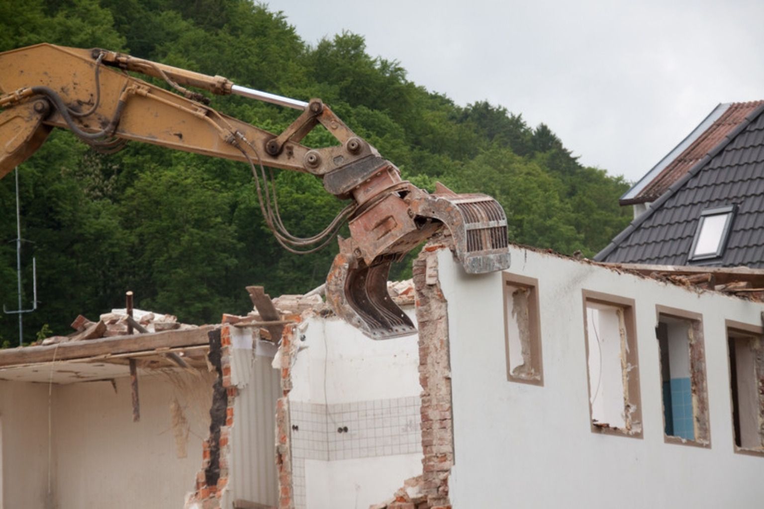 Gravemaskine med nedrivningsgrab river et hvidt hus ned