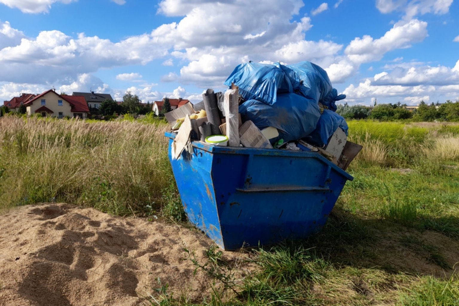 Blå container fyldt med affald på en grund med huse i baggrunden